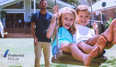 Man pushes two children on a swing in front of his home